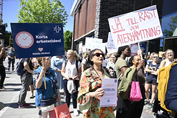En grupp människor protesterar på en gata och håller upp skyltar som förespråkar kortare arbetstider och raster. Vissa skyltar är på svenska, inklusive en med texten "Ja till rast och återhämtning".