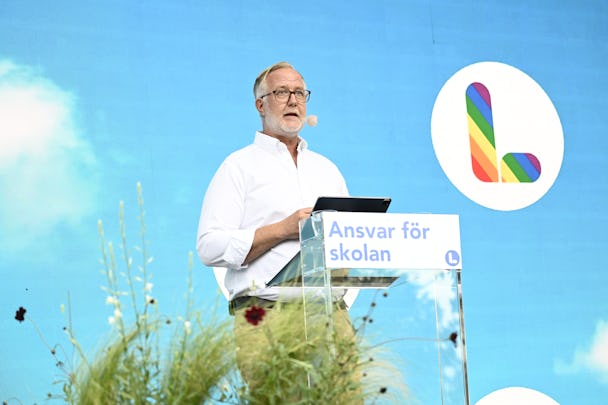 Johan Pehrson talar vid ett podium med en skylt som lyder "Ansvar för skolan" framför en blå bakgrund med en regnbågsfärgad L-logotyp.