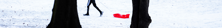 Ett barn drar en röd pulka i snön.