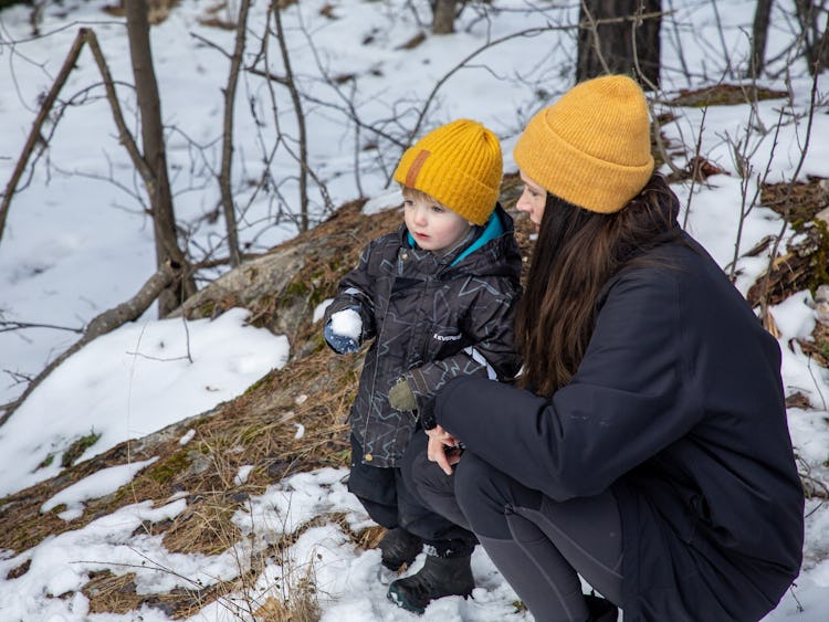 Ett barn och en förälder bär matchande gula mössor är utomhus i en snöig skogsmiljö.