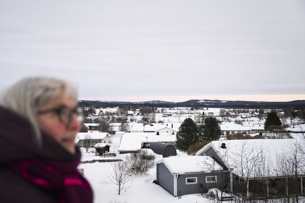 Kvinna stirrar på en snötäckt liten stad med kullar i fjärran.
