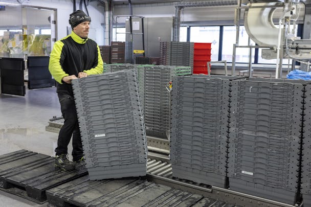 En arbetare flyttar staplar med plastlådor i en industriell miljö.
