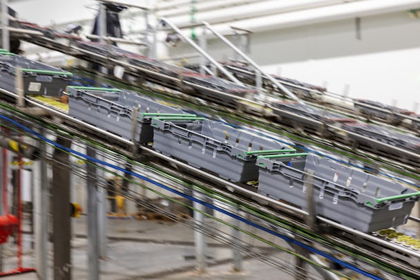 Transportbandsystem som flyttar gråa behållare genom en industriell anläggning.