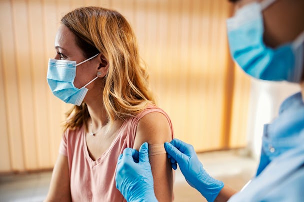 En nyvaccinerad kvinna med munskydd, och läkare som sätter ett plåster på hennes arm.