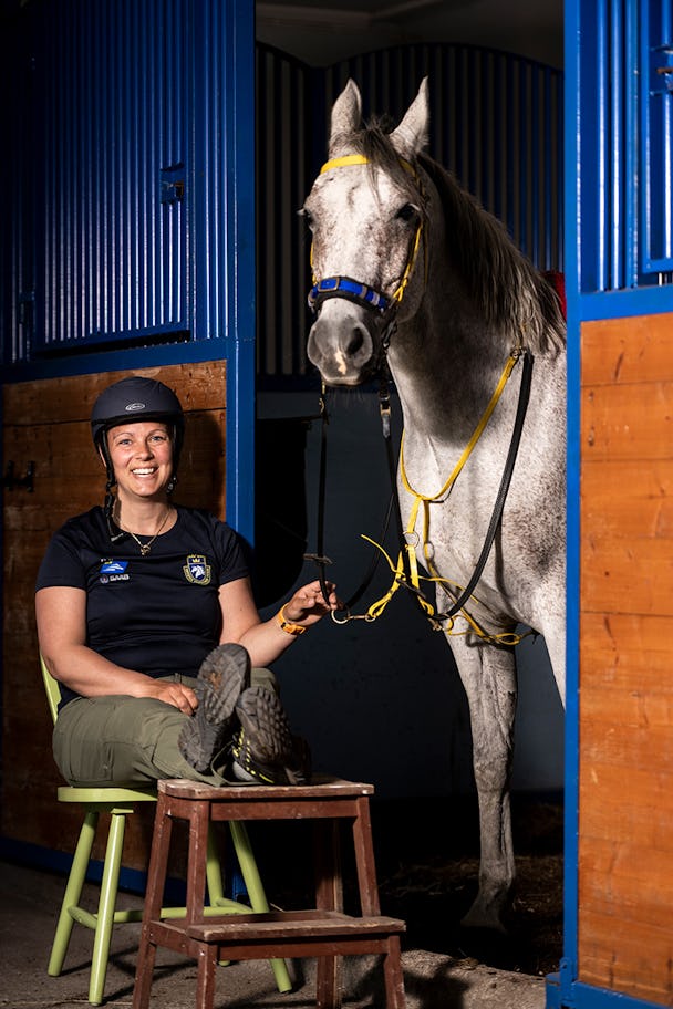 Frida Westerlund på en stol i stallet med hästen Kalle.