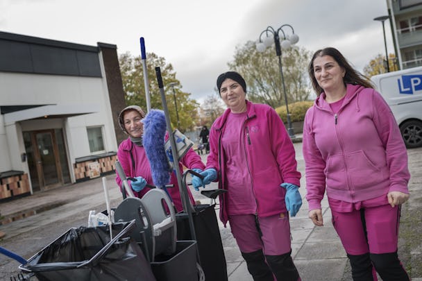 Zeliha Bulduk, Gülüzar Atik och Elife Demirci går utomhus i rosa arbetskläder och med en städvagn.