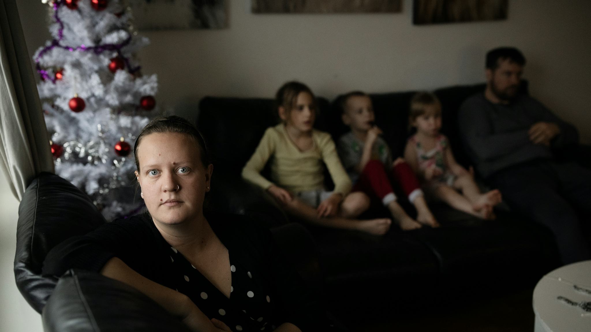 Jennifer Blomberg hemma i lägenheten. I bakgrunden sitter hennes tre största barn och en man i en soffa bredvid en julgran.