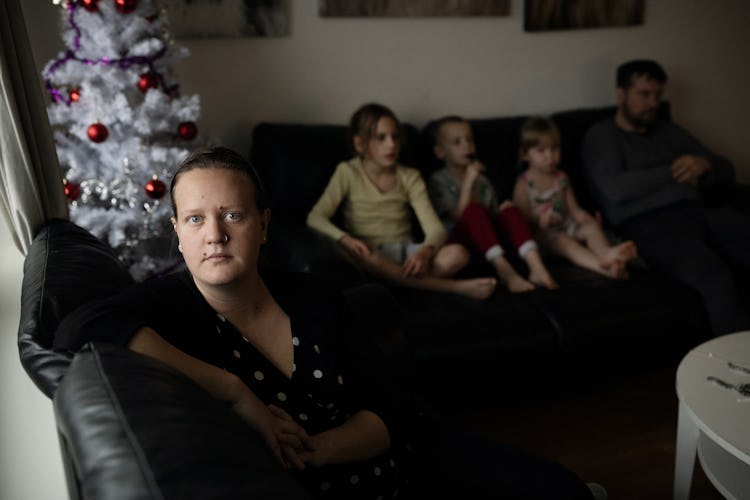 Jennifer Blomberg hemma i lägenheten. I bakgrunden sitter hennes tre största barn och en man i en soffa bredvid en julgran.
