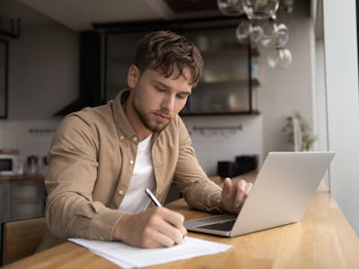 En man sitter vid ett bord med en bärbar dator och en penna.