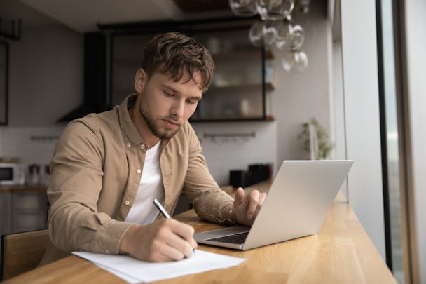 En man sitter vid ett bord med en bärbar dator och en penna.