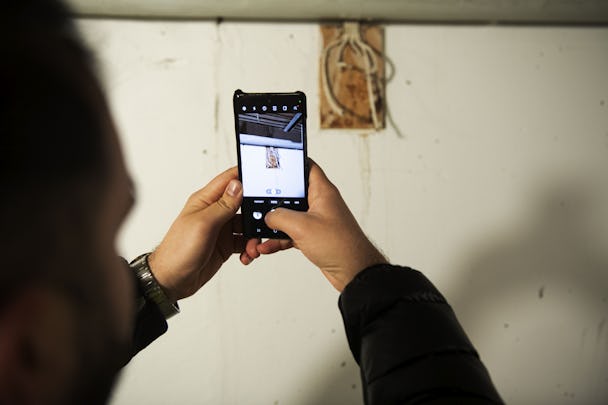 En man tar en bild av kablar som sticker ut ur väggen med en mobiltelefon.