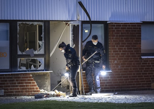 Bild på två poliser som undersöker ett krossat fönster på en tegelbyggnad.