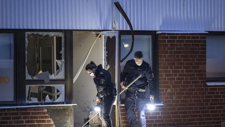 Bild på två poliser som undersöker ett krossat fönster på en tegelbyggnad.