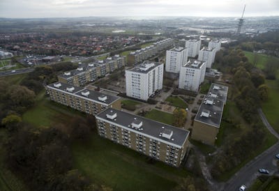 Bild på ett bostadsområde sett från ovan med flera höghus omgivna av grönområden och vägar, under en molntäckt himmel.