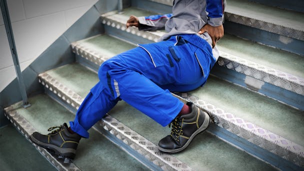 Person i blå arbetskläder och svarta stövlar som sitter på trappor, ser ut som om han har ramlat.