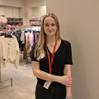 En ung kvinna som står framför ett ställ med kläder.