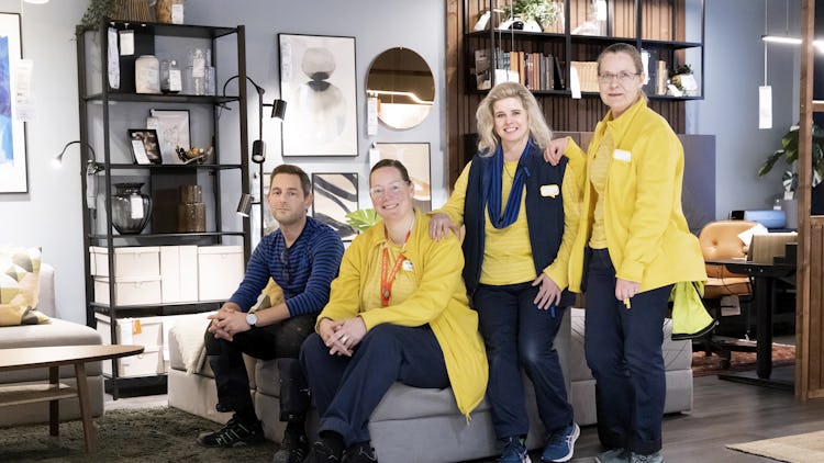 En grupp människor i gula jackor poserar i en möbelbutik.