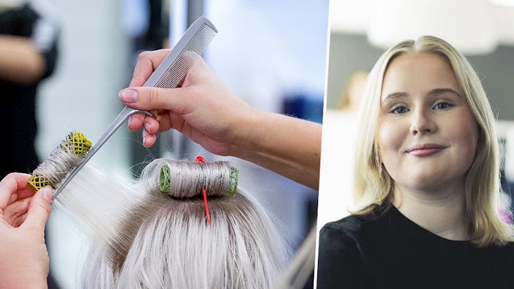 En frisör jobbar på en kvinnas hår med rullar och en kam i en salong.