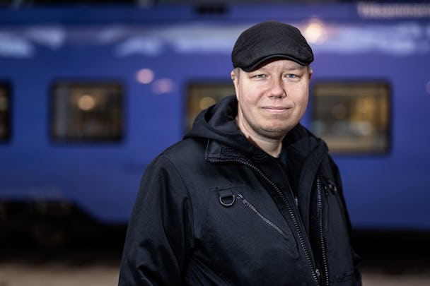 Ola Brunnström i keps framför ett blått tåg från Pågatågen.