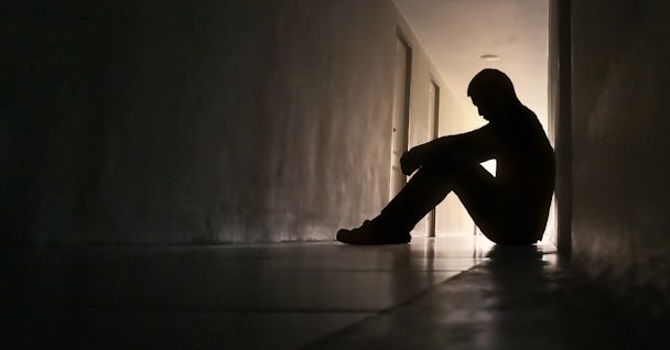 Person i siluett sitter ensam på ett golv i en mörk korridor.