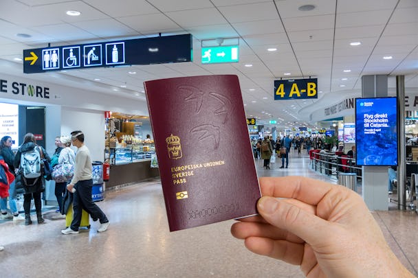 Monterad bild. En hand håller i ett svensk pass av 2022 års modell. I bakgrunden en massa folk någonstans på Arlanda flygplats.