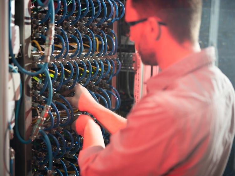 En man står och undersöker kablar medan han reparerar en server. Lön: Vad tjänar en fibertekniker?