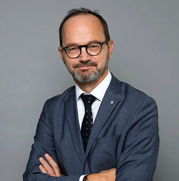 Porträttbild på Tomas Eneroth i mörkblå kostym, vit skjorta och mörk slips