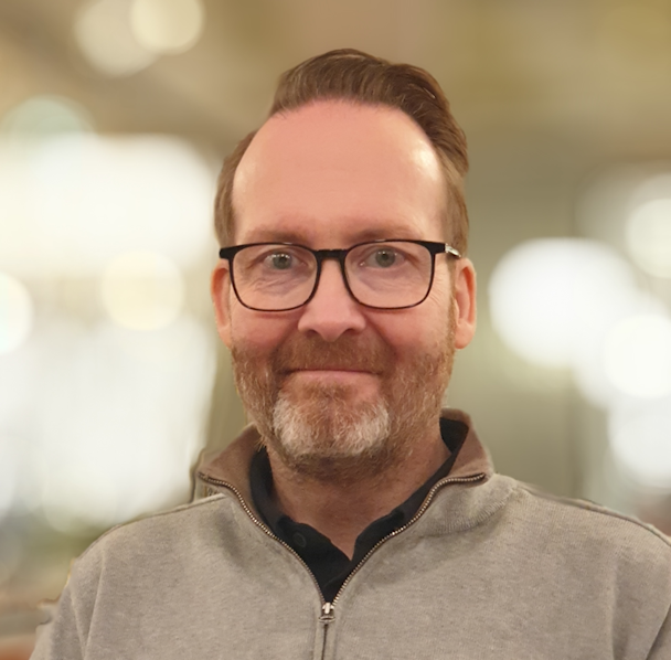 Porträttbild på Patrik Allinger i en gråbeige tröja.