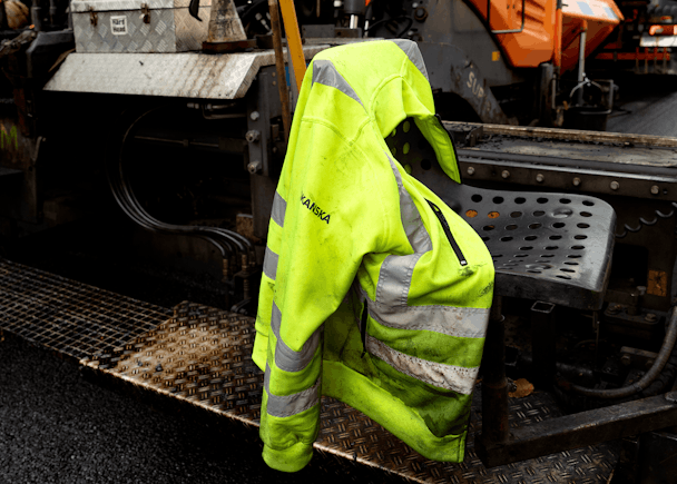En gul varseljacka hänger på ett fordon som används för beläggningsarbete.