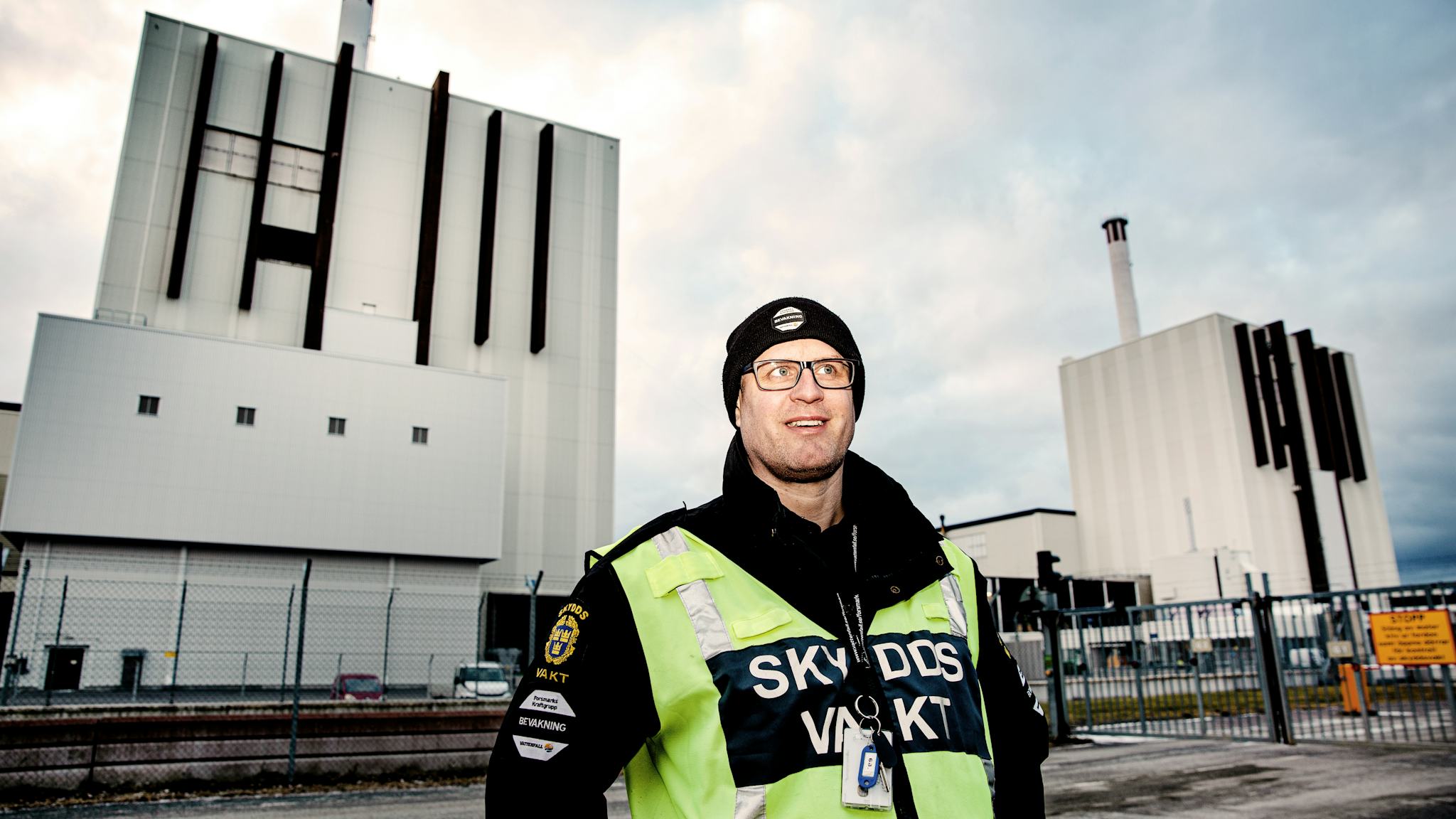 Skyddsvakten Henrik i gul varselväst framför Forsmarks reaktor 1. I bakgrunden syns även grinden in till reaktorområdet.
