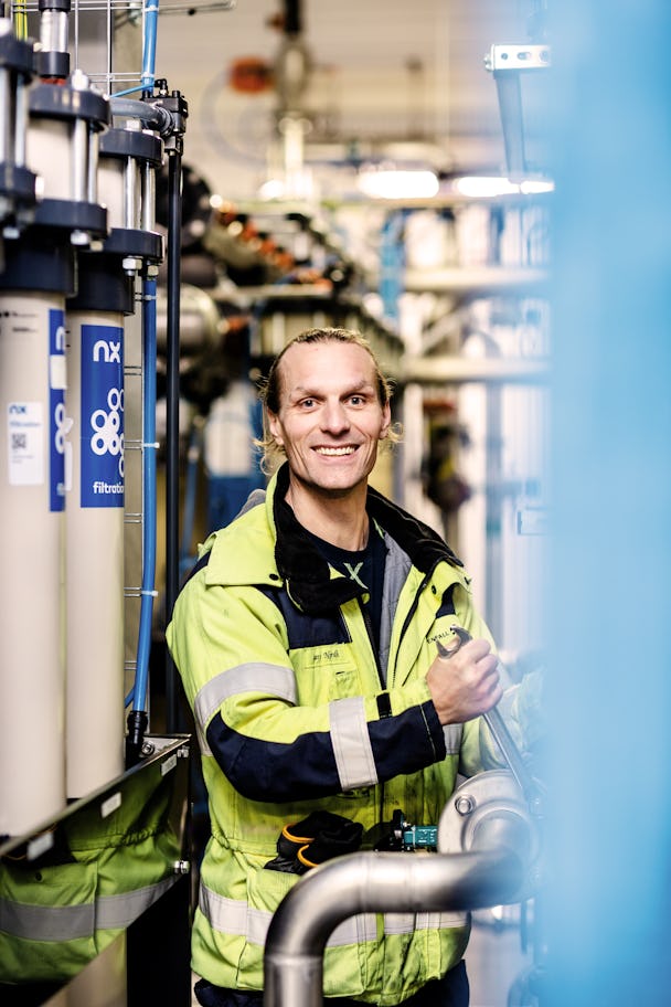 Underhållsteknikern Lars Nordh med en stor skiftnyckel inuti en av kärnkraftverkets byggnader, där han kollar ett rör. Han tittar leende in i kameran.