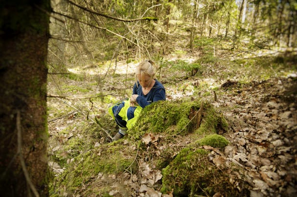Fältteknikern Lotta Hermond på huk i skogen, dold av en sten.