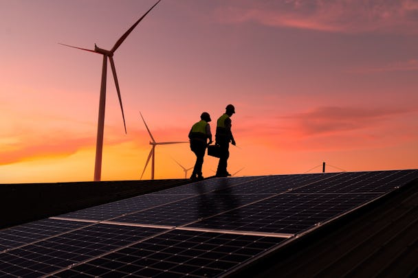 Genrebild på två personer framför solceller och vindkraftverk.
