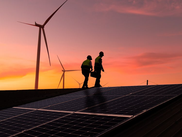 Genrebild på två personer framför solceller och vindkraftverk.