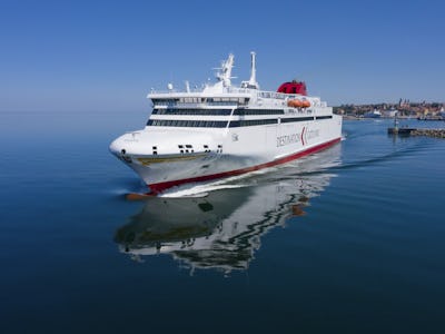 En vit och röd färja från Destination Gotland färdas över Östersjön med Visby i bakgrunden.
