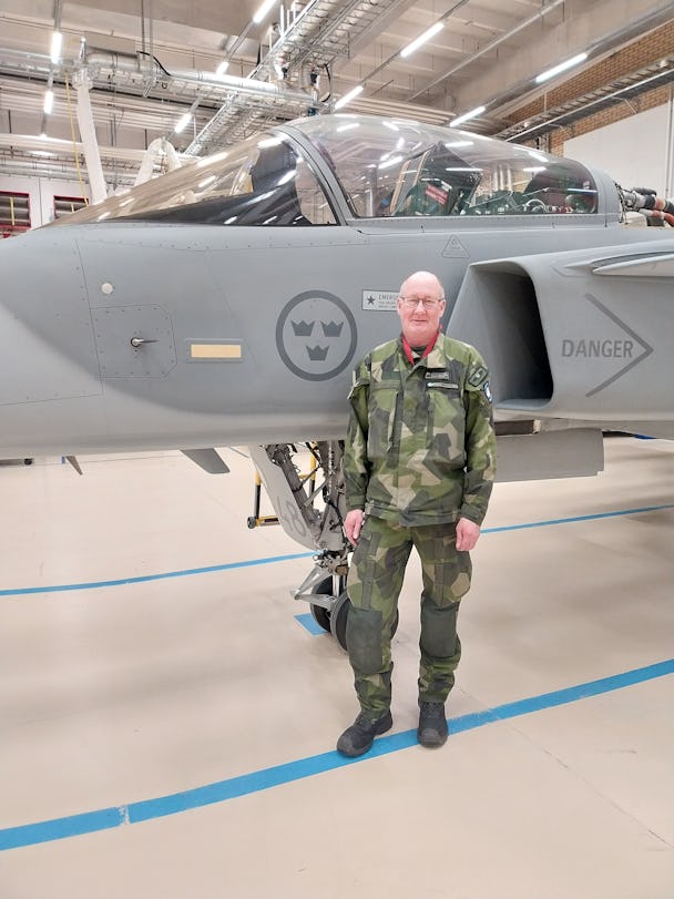 Lars Bäckström, flygtekniker på Försvarsmakten, står i kamouflagekläder framför ett stridsflygplan.