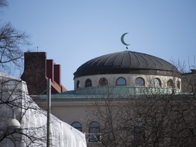 Kupol av en moské med en halvmåne synlig mot en klar himmel, inramad av omgivande byggnader och träd.