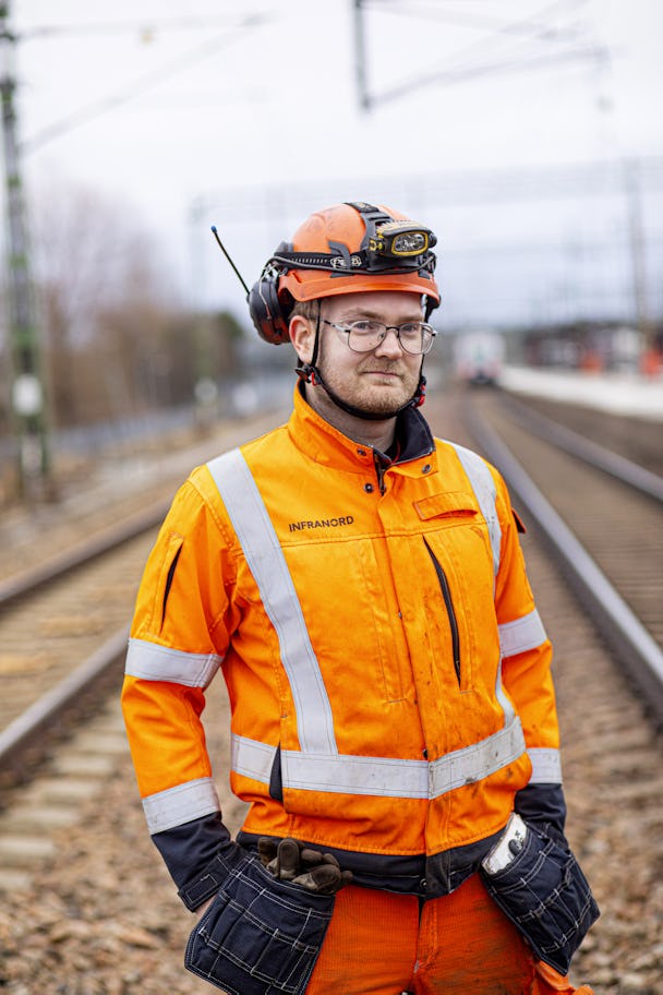 Porträtt på Kenneth Nilsson i hjälm och orange arbetskläder med järnvägsspår i bakgrunden.