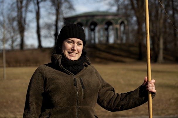 Carolina Mellblom står framför en grön paviljong med en räfsa i handen.