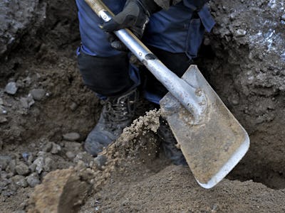 En arbetare gräver i jorden med en spade.