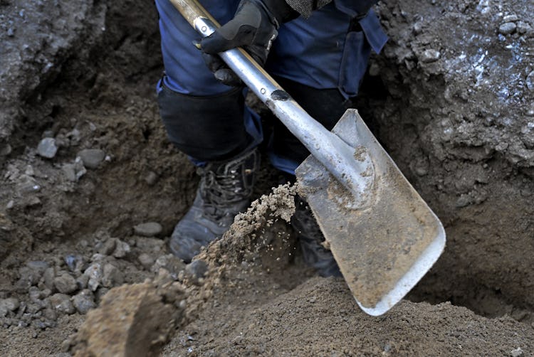En arbetare gräver i jorden med en spade.