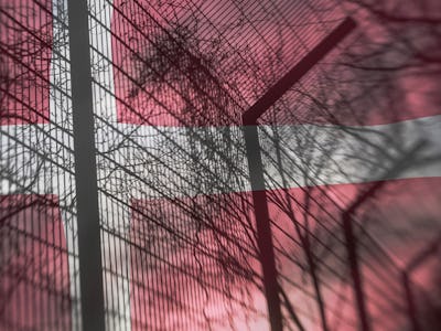 Ett stängsel vid ett danskt fängelse med en dansk flagga i bakgrunden.