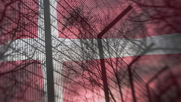 Ett stängsel vid ett danskt fängelse med en dansk flagga i bakgrunden.