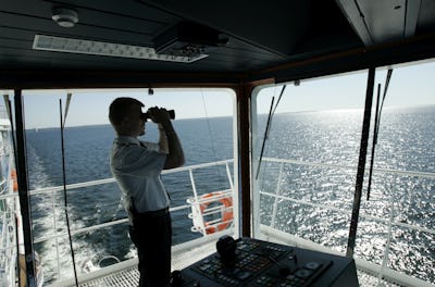 En person i uniform använder en kikare för att titta ut över havet från ett fartygs brygga.
