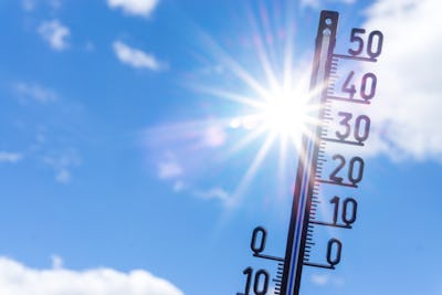 En utomhustermometer visar en temperatur som stiger mot 50 grader. Solen lyser och det finns några moln på en blå himmel.