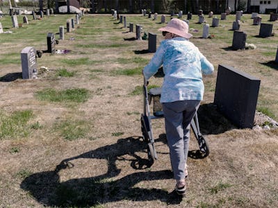 Äldre kvinna med rullator, går bland gravstenar.