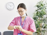 Undersköterska i rosa kläder tittar på sin klocka.
