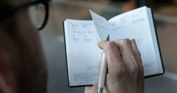 En man som skriver i en fickkalender med en penna.