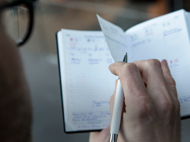 En man som skriver i en fickkalender med en penna.