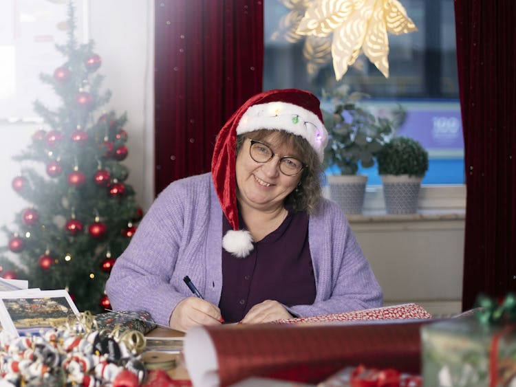 Mona Burås Dieng i en tomtehatt som sitter vid ett skrivbord och slår in julklappar till sina kollegor.